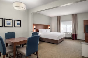 Una habitación de hotel con cama, escritorio, sillas, lámpara y cuadros en la pared.