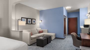 A hotel room with a bed, a sofa, a desk, a chair, and a small table.