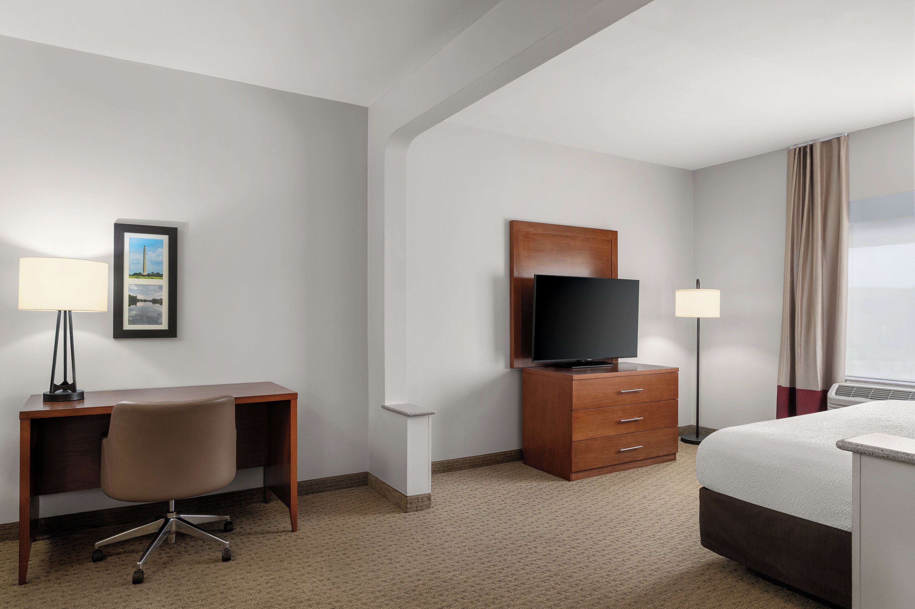 A hotel room with a desk, chair, television, and a bed.