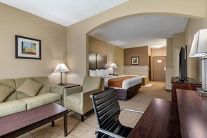 A hotel room with a sofa, armchair, dining table, and a bed with a headboard. - Comfort Suites The Colony - Plano West (The Colony)