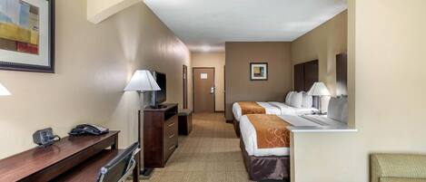 Habitación de hotel con escritorio, dos camas, una silla, televisor y lámpara.