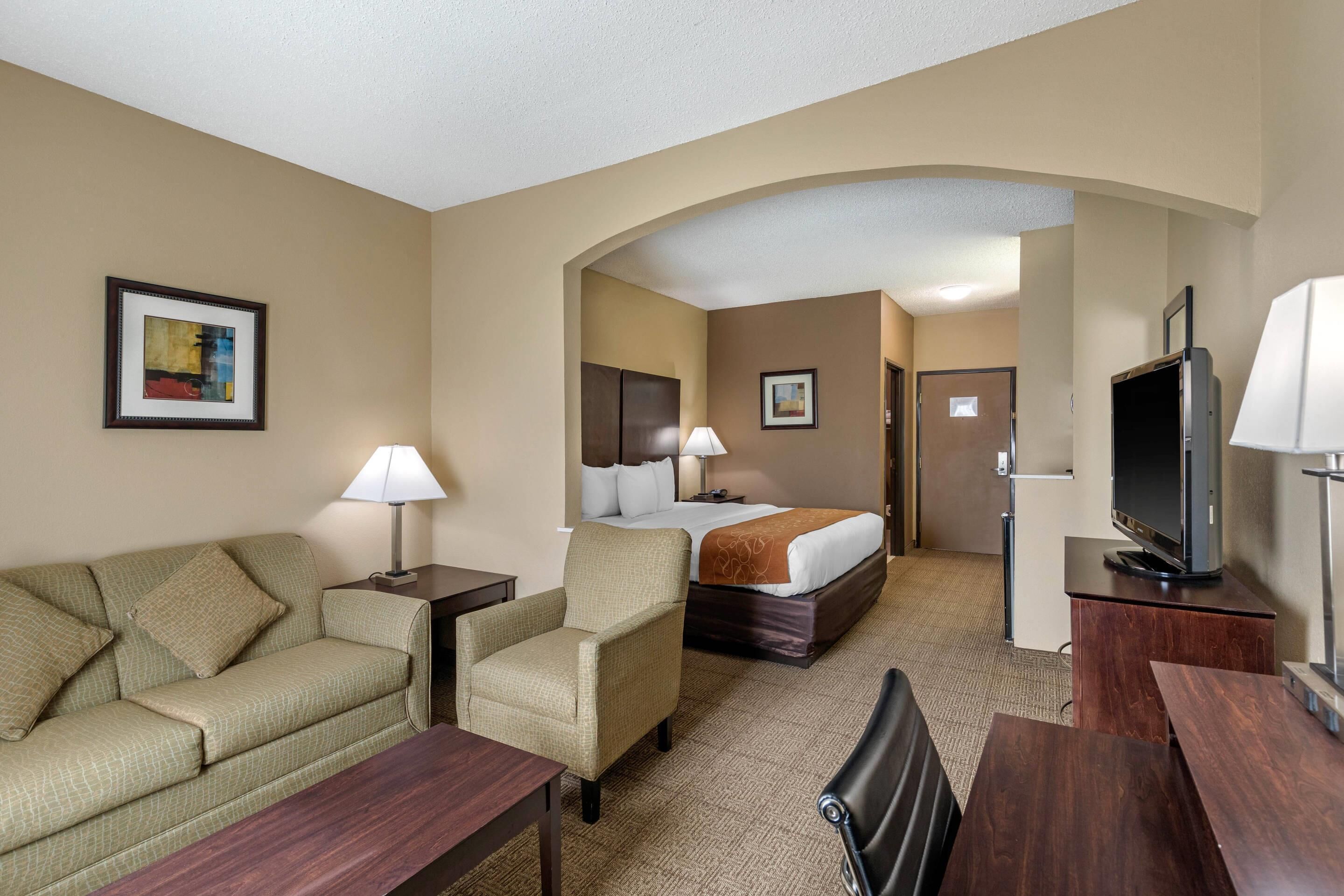 Una habitación de hotel con sofá, sillón, cama, televisor y escritorio.