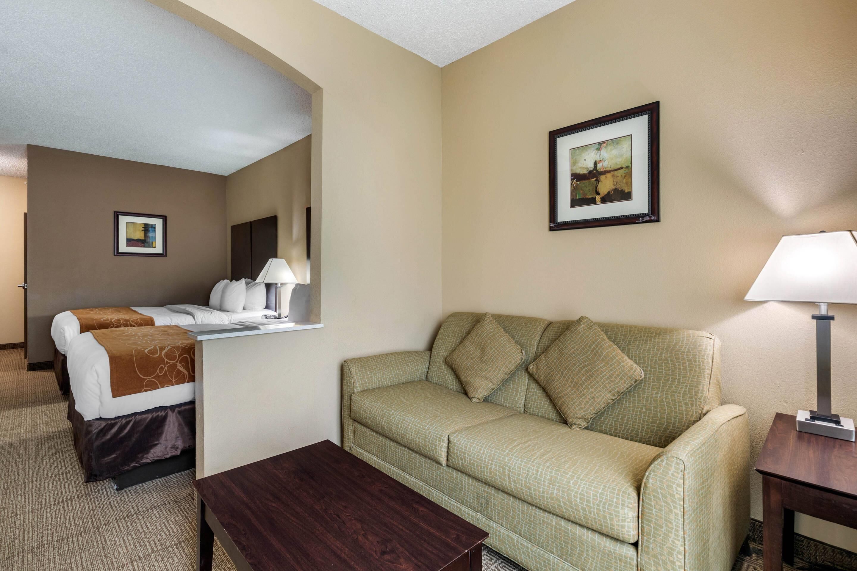 A hotel room with a bed, a sofa, a coffee table, a lamp, and a framed picture on the wall.