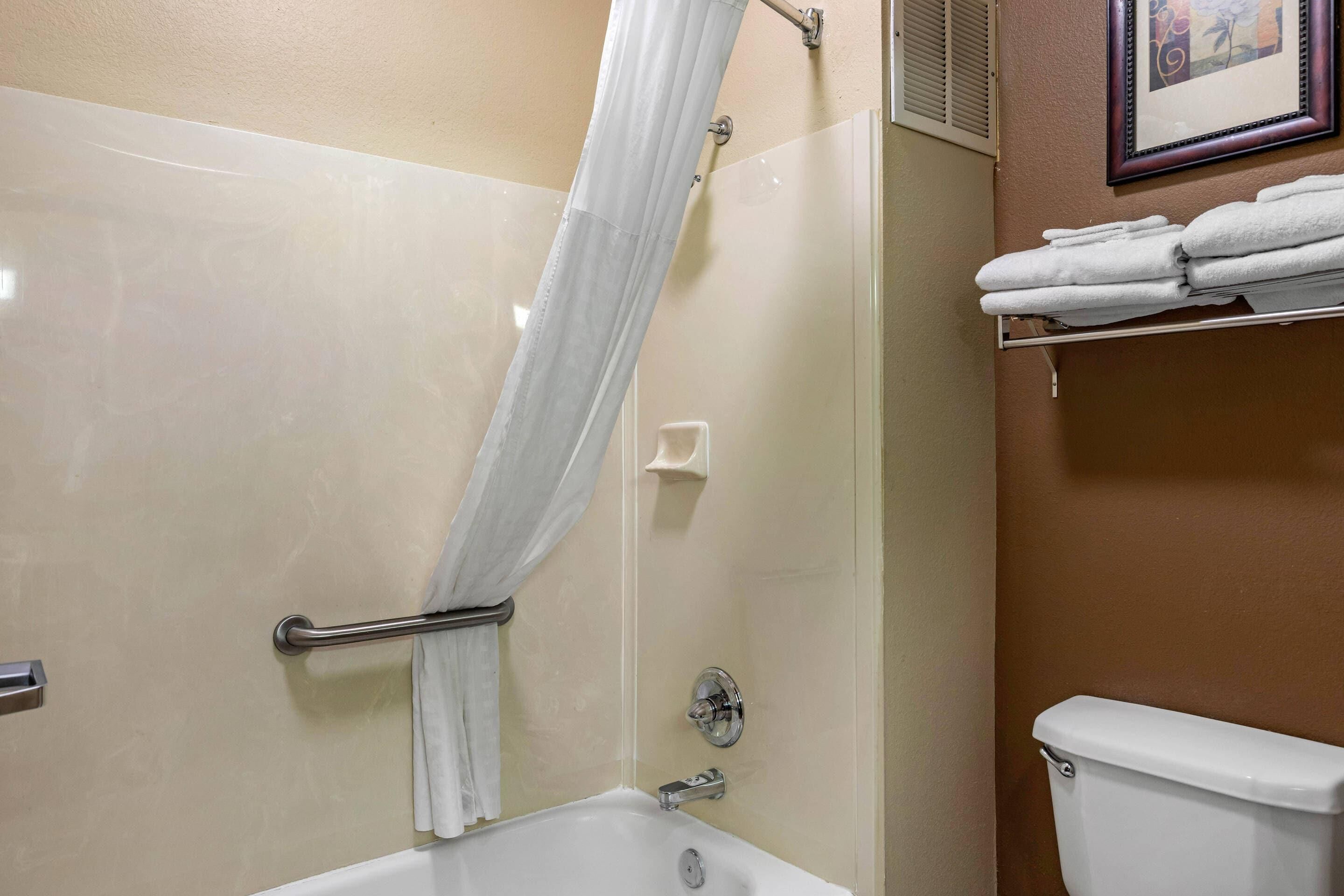 A bathroom with a bathtub, a shower curtain, a toilet, and a towel rack with towels.