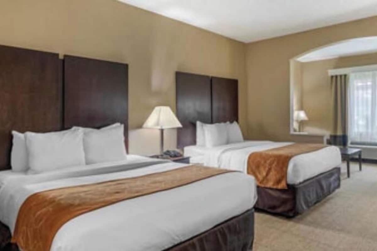 A hotel room with two beds, a desk, a chair, and a window with curtains.