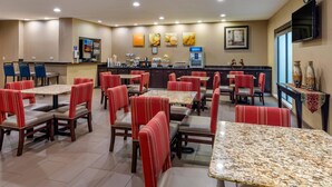 Un restaurant avec des banquettes rouges en tissu et des tables en granit, un appareil à café et un téléviseur fixé au mur.