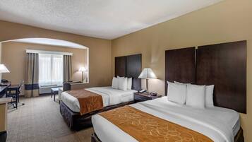 Habitación de hotel con dos camas, un escritorio, una silla y un ventanal con cortinas.