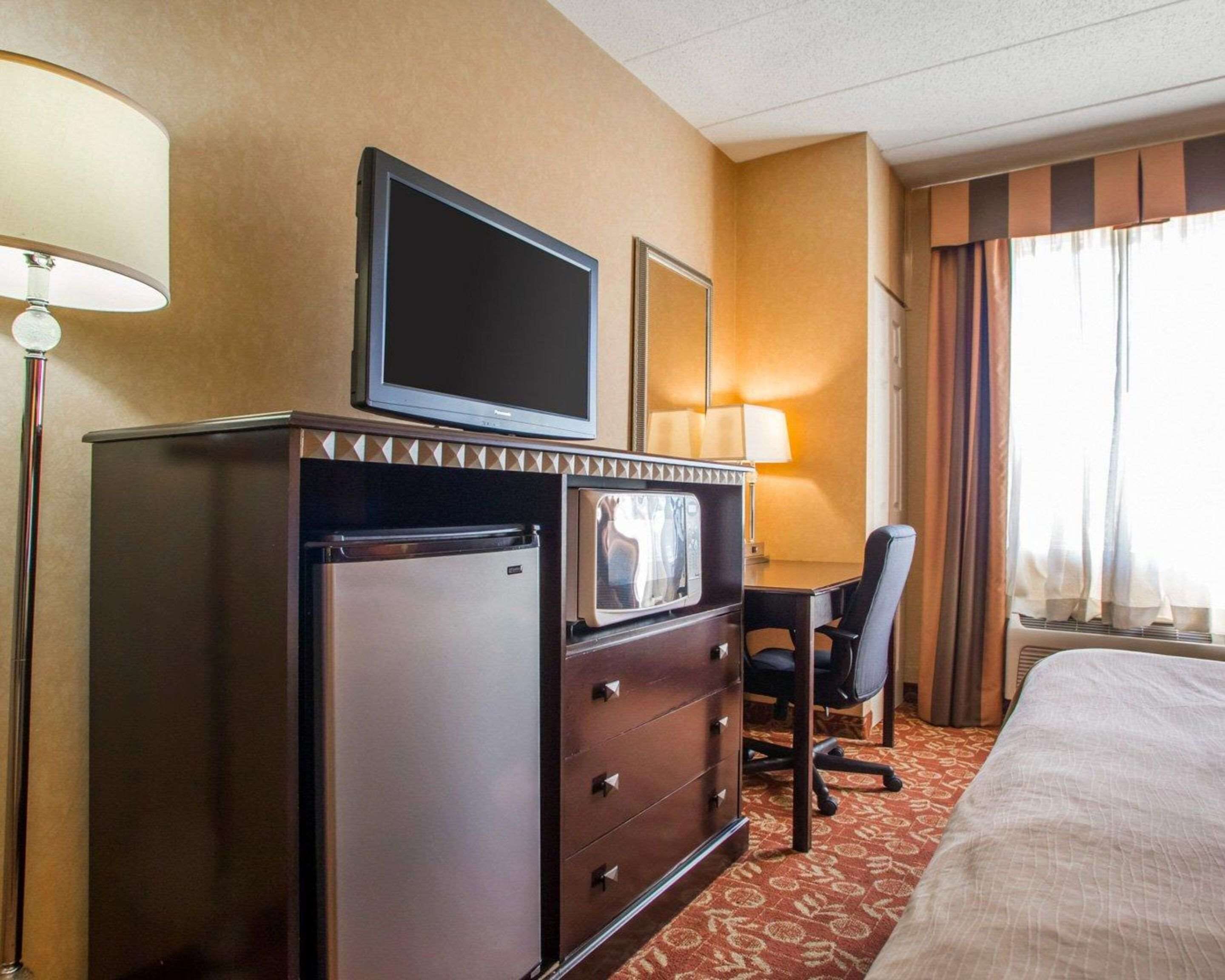 Habitación de hotel con cama, escritorio con silla, televisor, refrigerador y lámpara.