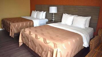 A hotel room with two beds, a nightstand with a lamp, and a patterned carpet.