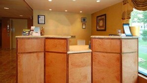 Un espace d’accueil avec un comptoir de réception en bois, des tableaux encadrés au mur et une fenêtre donnant sur l’extérieur.