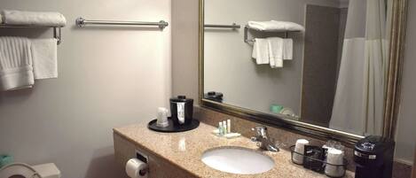 Un baño de hotel con lavamanos, espejo, toallero, inodoro y cafetera.