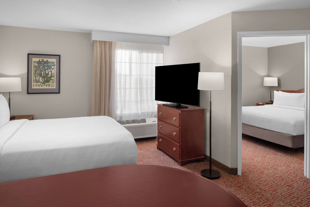 Een hotelkamer met twee bedden, een flatscreen-tv, een dressoir en een groot raam met dunne gordijnen.