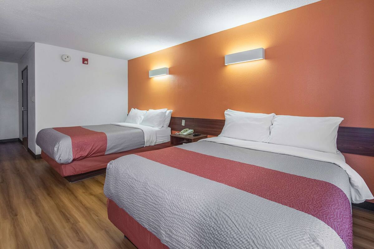 A hotel room with two beds, wooden flooring, and a red-orange wall.