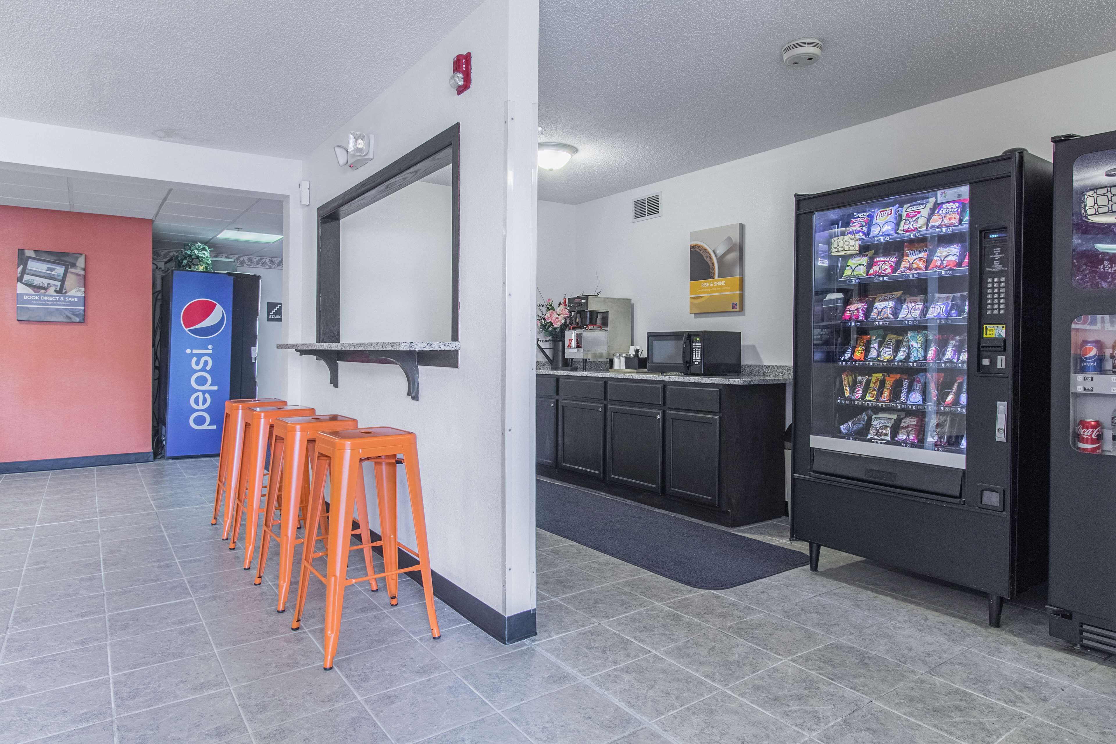 A lobby with a Pepsi sign, a vending machine, and orange stools.
