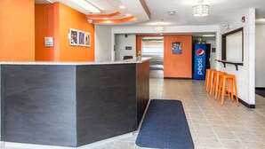 A reception area with a dark reception desk, orange walls, and a Pepsi sign. There are orange stools and a blue mat on the floor.