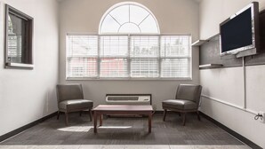A room with a large window, two chairs, a table, and a mounted TV.