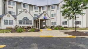 A multi-story hotel with a covered entrance, a parking lot, and a landscaped area with plants.