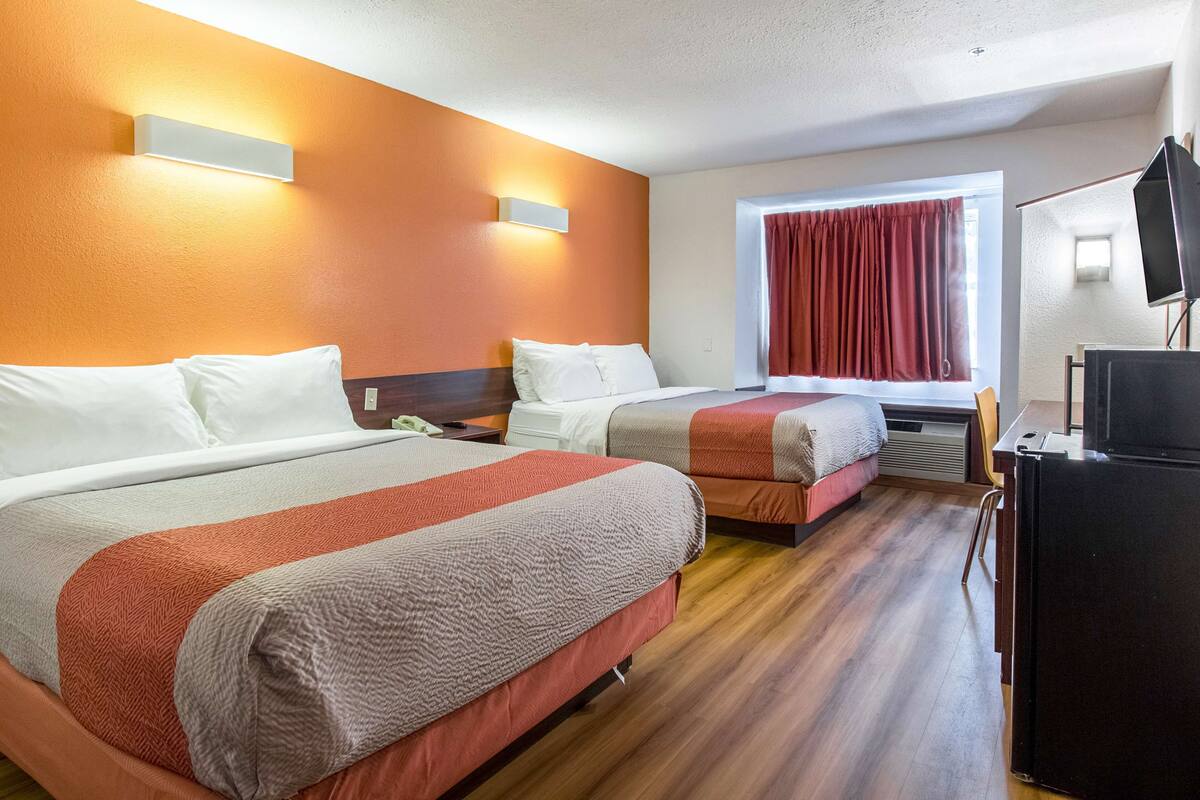 A hotel room with two beds, a television, and a window with curtains.