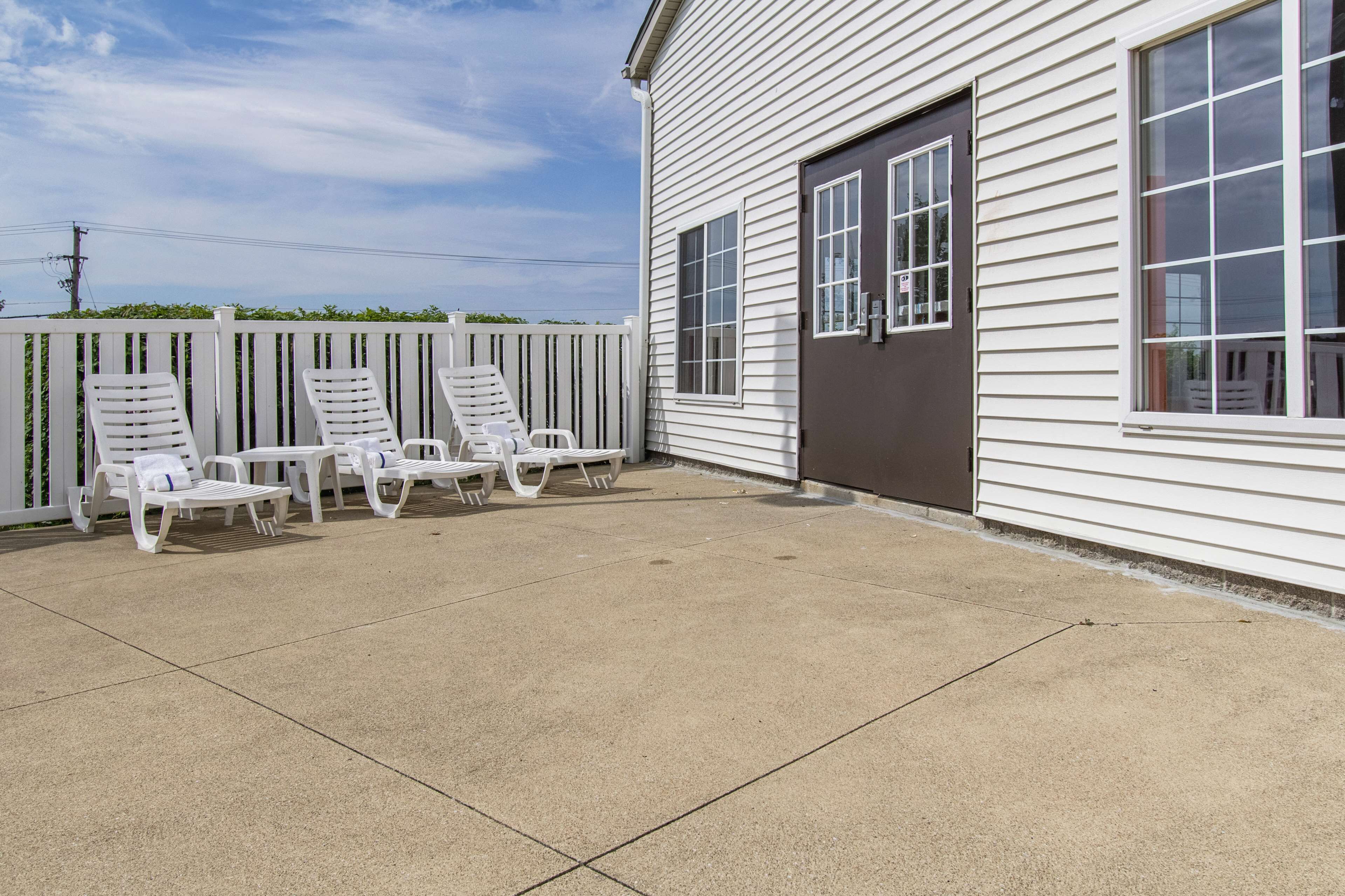 A covered patio area with white lounge chairs and a concrete floor.