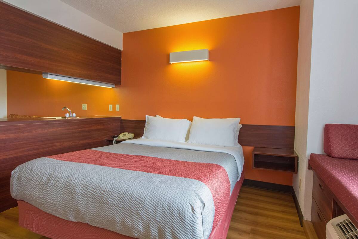 A hotel room with a large bed, a bedside table, a nightstand, a mirror, and a red chair.
