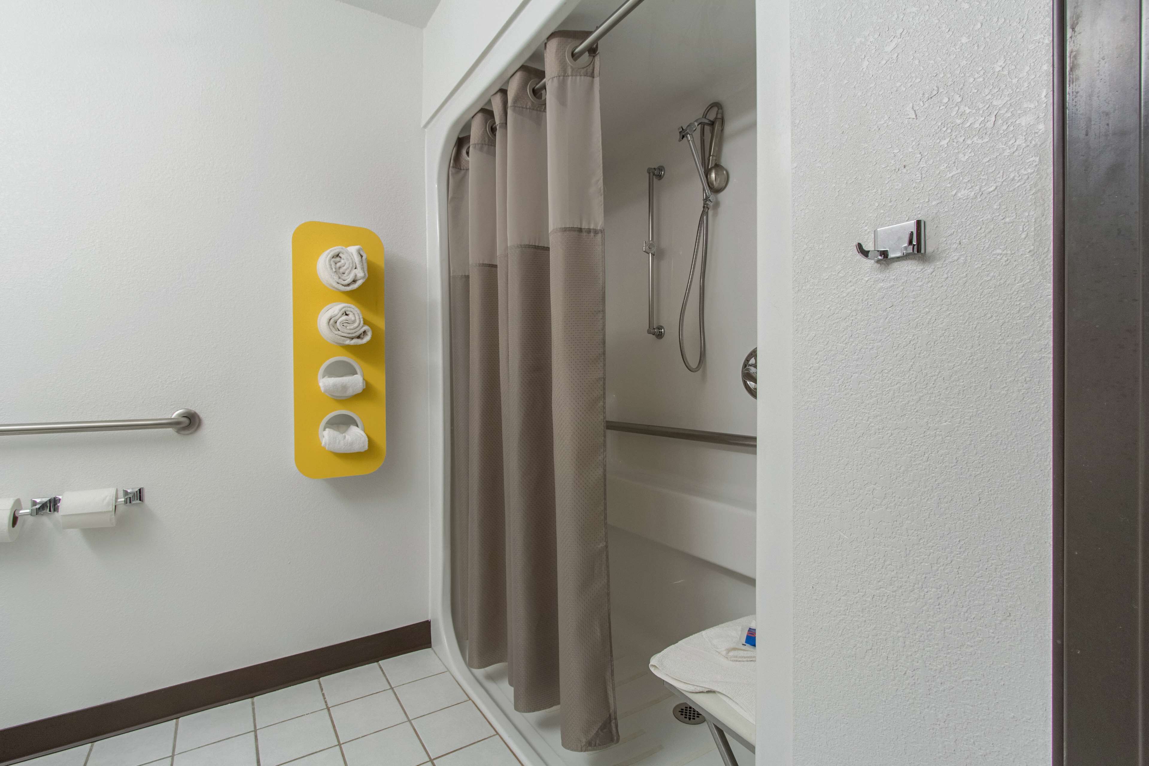 Een badkamer met een toiletrolhouder, een handdoekrek met handdoeken, een douchegordijn en een douchekop.