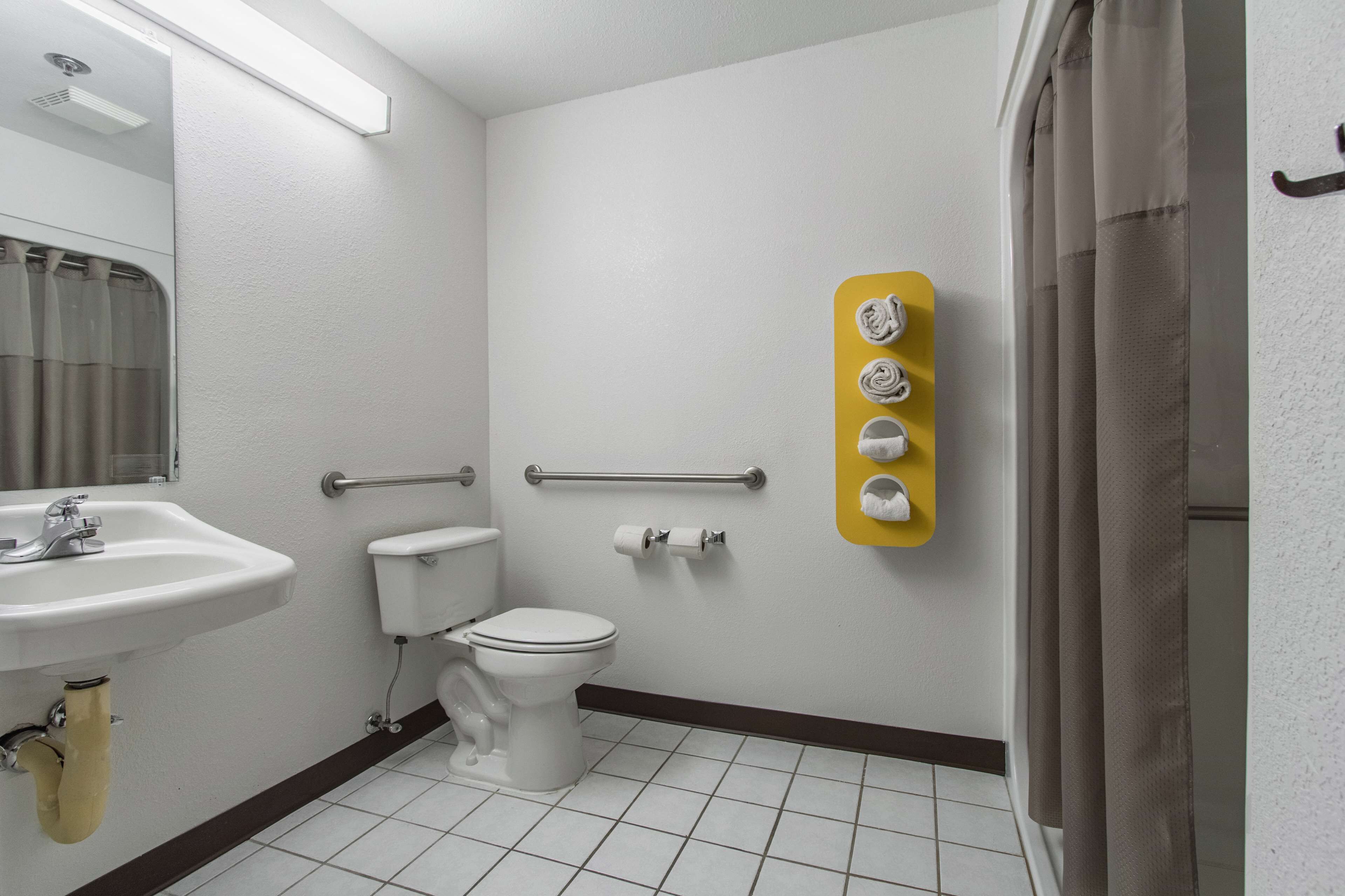 Casa de banho com lavatório branco, sanita e cortina de chuveiro. Há um porta-toalhas amarelo com quatro toalhas.