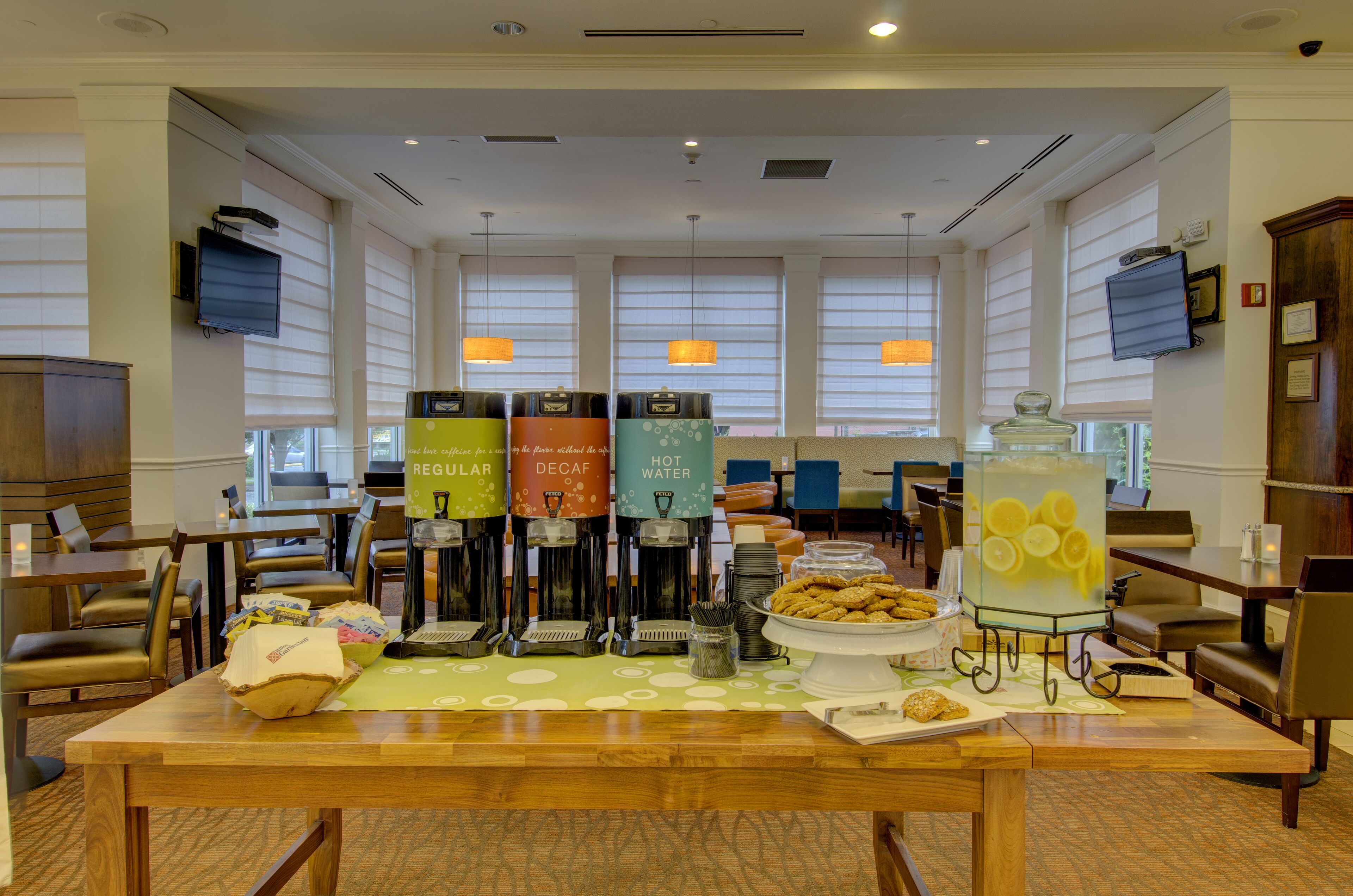 Zona de desayuno de hotel con cafeteras, una presentación de frutas y arreglos de asientos.