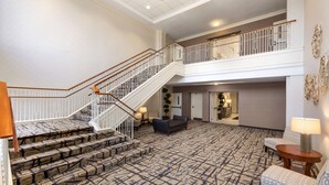 A spacious lobby with a patterned carpet, a staircase with wooden railings, and a seating area with a lamp. - Hilton Garden Inn Shelton (Shelton)