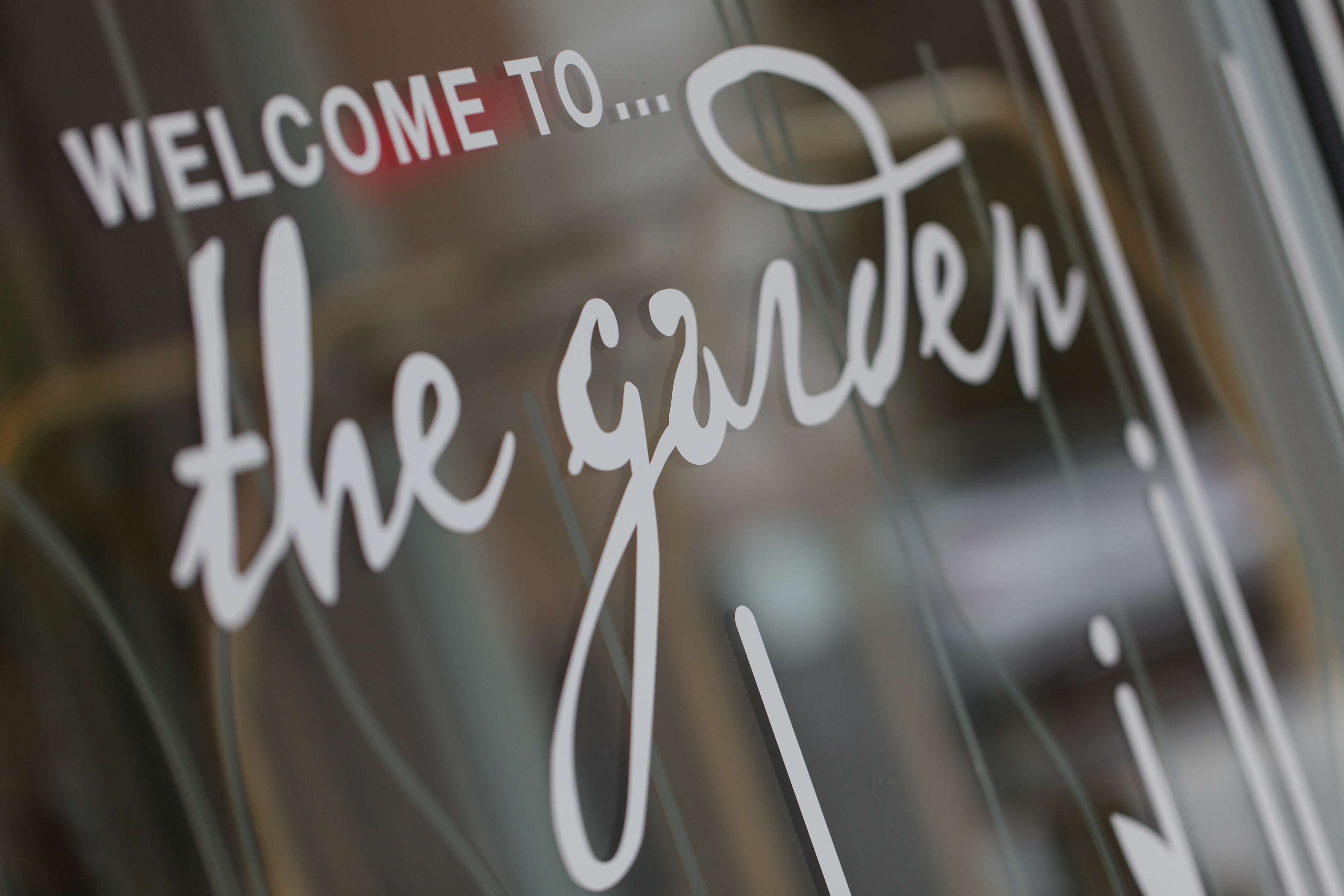 A close-up of a sign with the text "WELCOME TO... the garden!"
