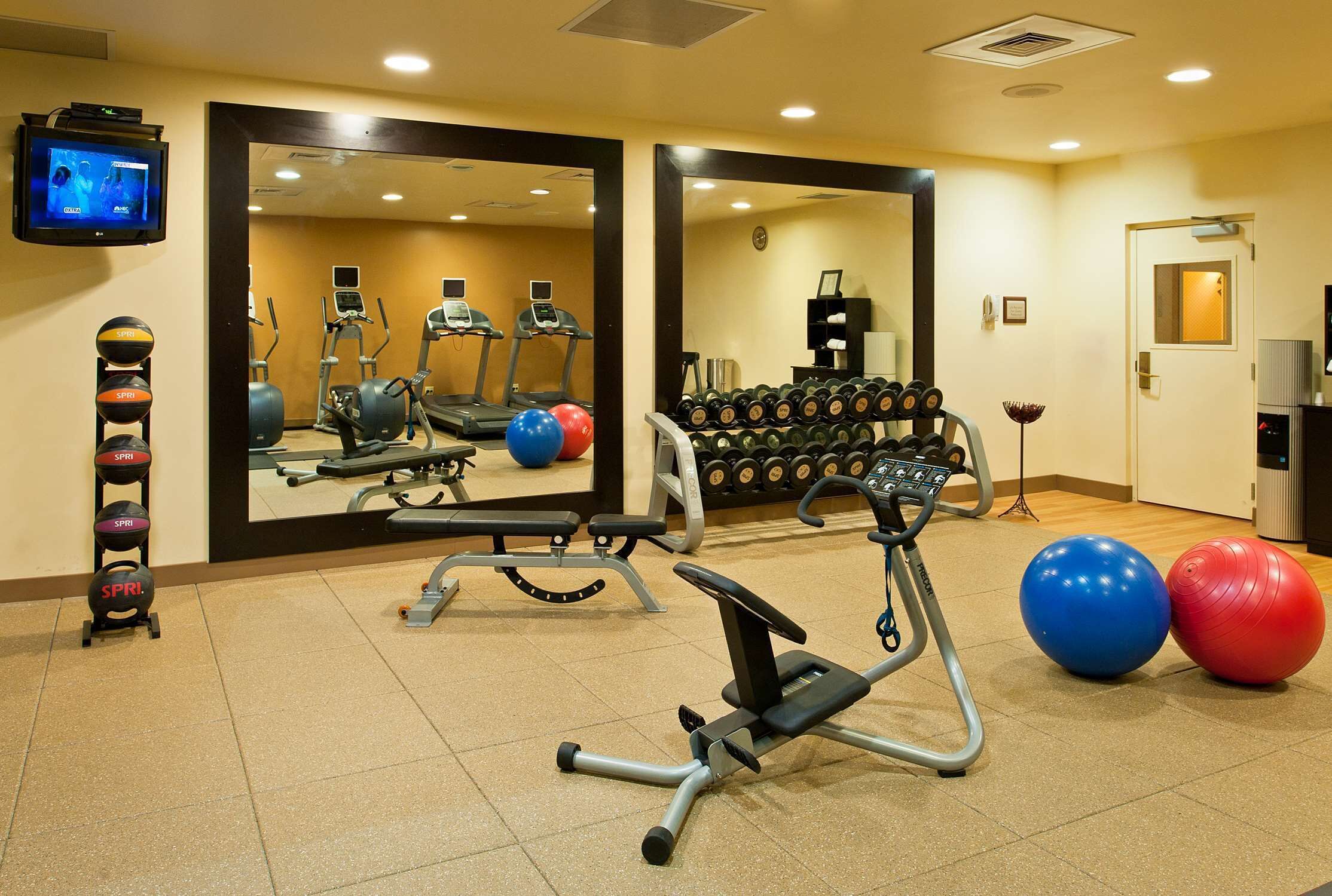 A gym with exercise equipment, a treadmill, and a mirror reflecting the space.