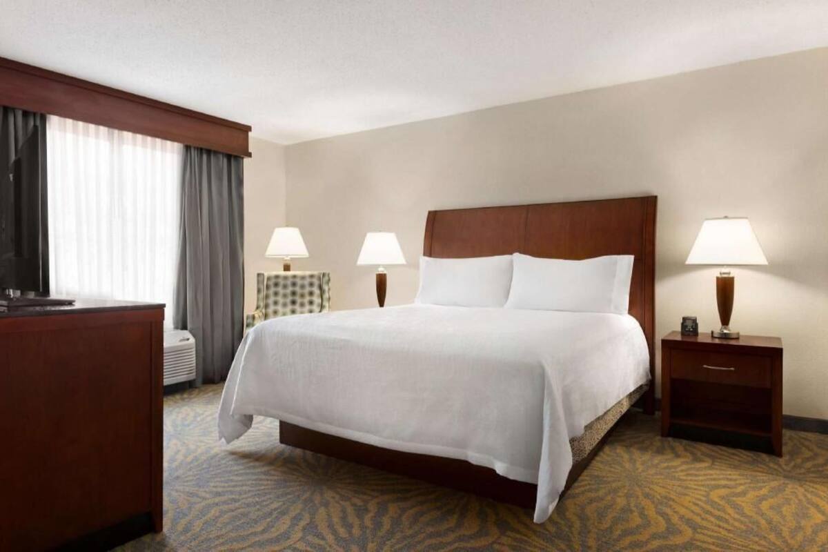 A hotel room with a large bed, two bedside lamps, a desk, and a window with curtains.