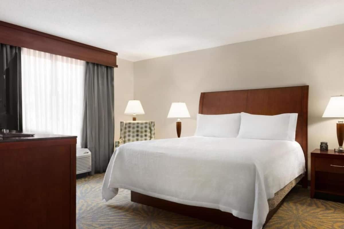 A hotel room with a large bed, two bedside lamps, a desk, and a television.