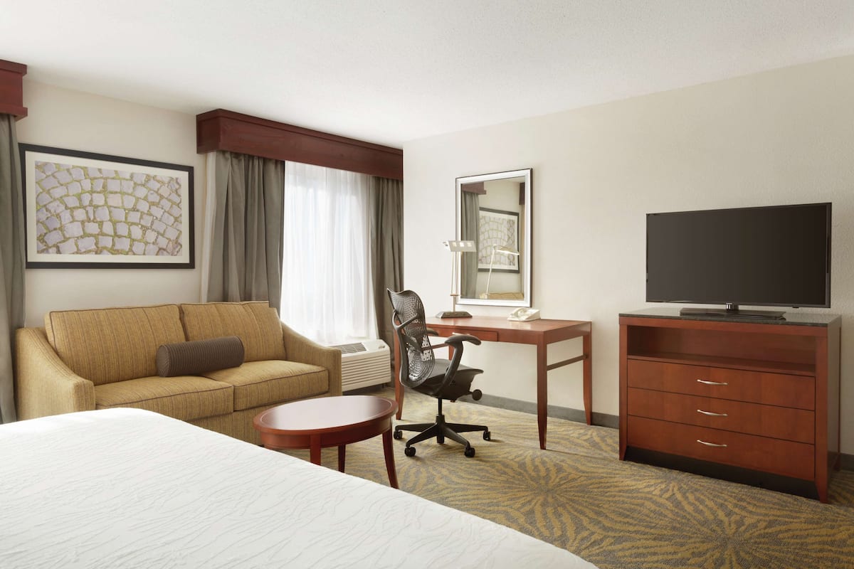 A hotel room with a bed, a sofa, a desk, a chair, a television, and a dresser.