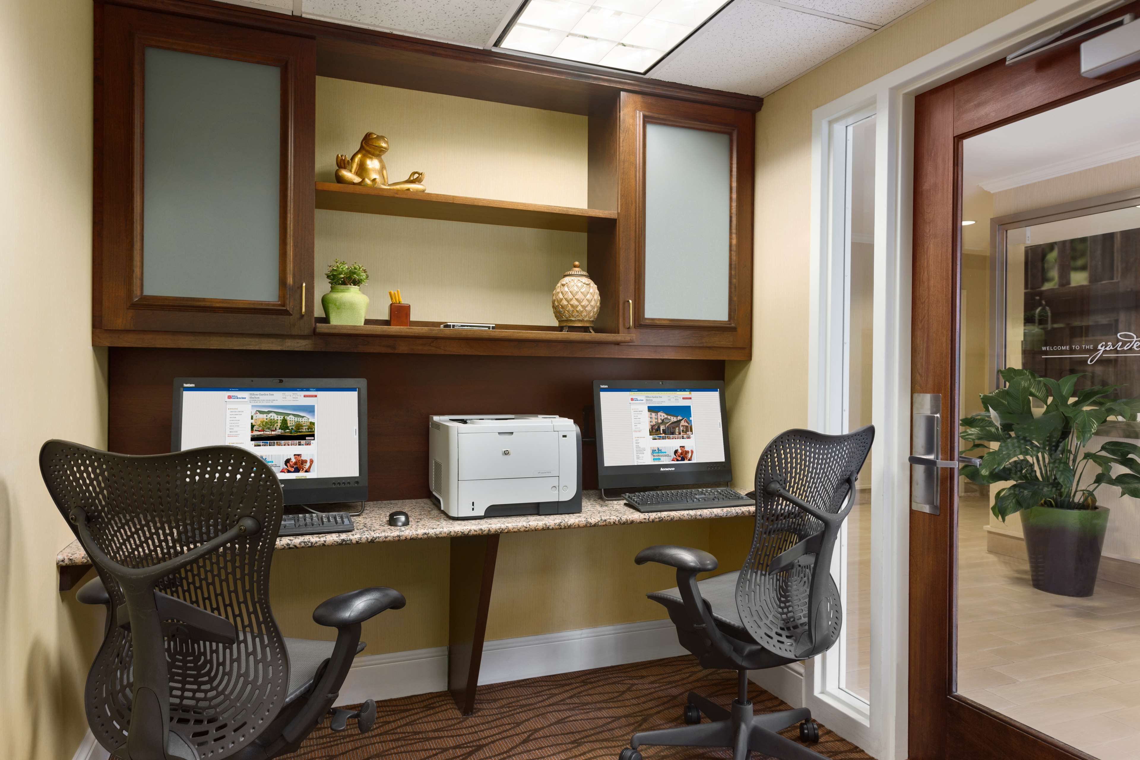 A workspace with two office chairs, a desk with two monitors and a printer, and a cabinet above the desk.