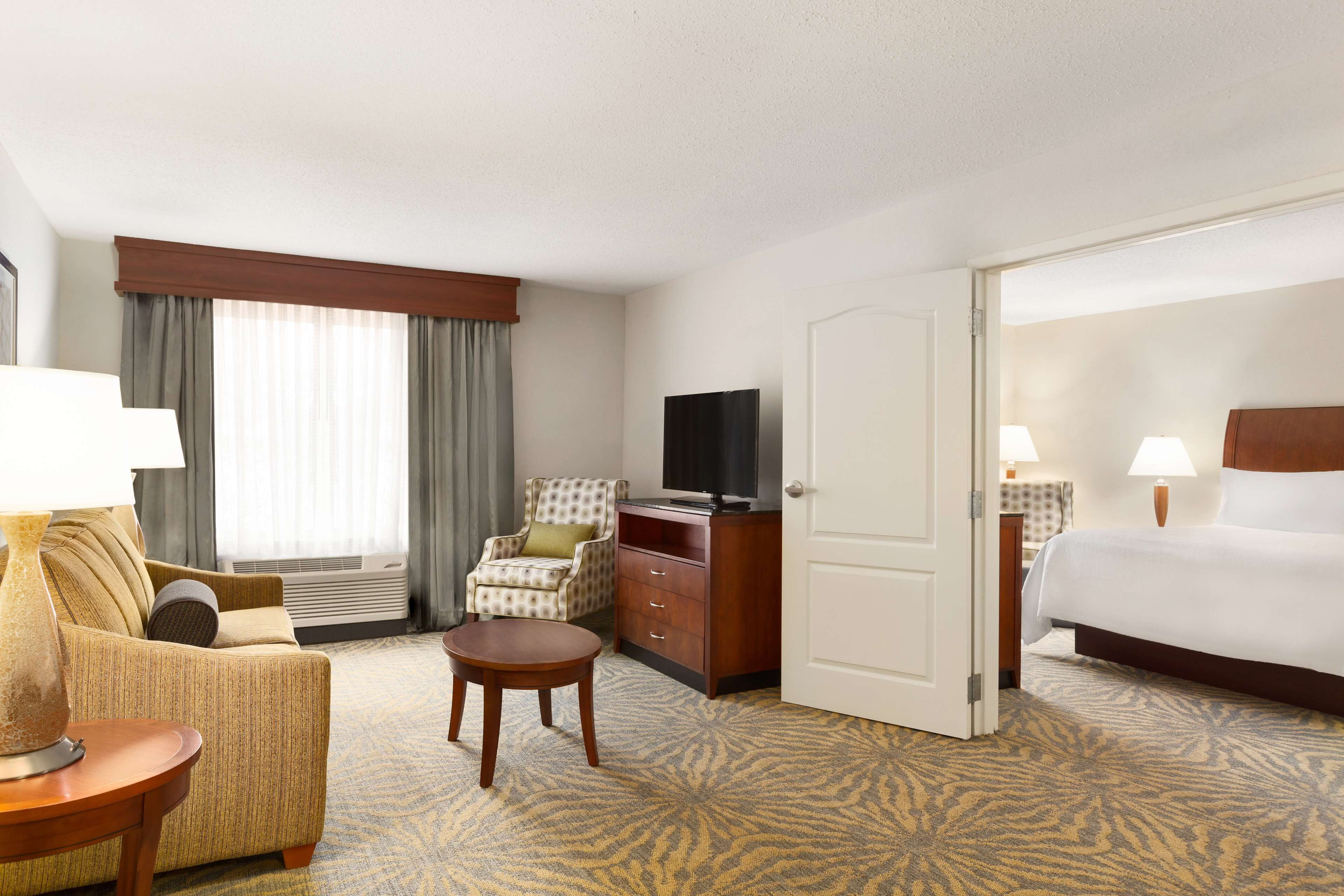 A hotel room with a bed, a sofa, a chair, a TV, a desk, and a carpeted floor.