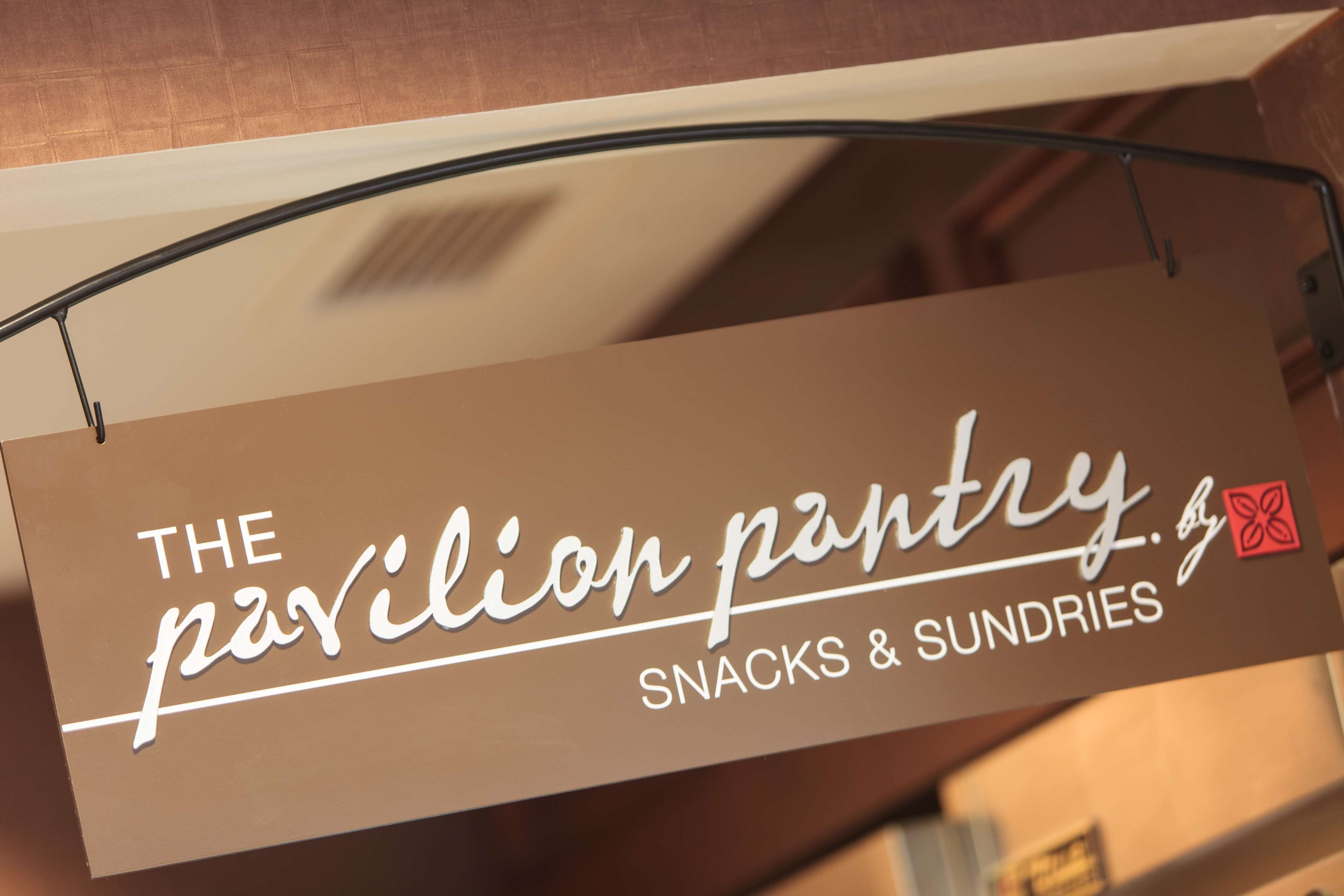 Skilt for 'The Pavilion Pantry' med logo og tekst, der angiver at det tilbyder snacks og diverse varer.