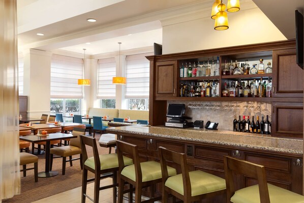 A bar area with a long counter, multiple seating options, and a variety of liquor bottles. - Hilton Garden Inn Shelton (Shelton)