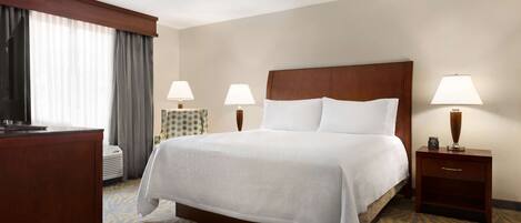 A hotel room with a large bed, two bedside tables with lamps, a desk, and a window with curtains.
