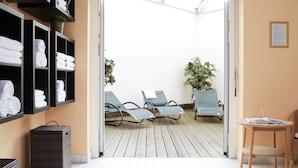 Un vestíbulo de hotel con una recepción, una zona de estar con sillones, un estante con toallas y una planta en maceta.