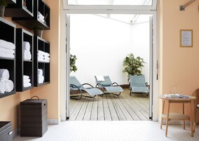 A hotel lobby with a reception desk, a seating area with lounge chairs, a wall-mounted shelf with towels, and a potted plant.