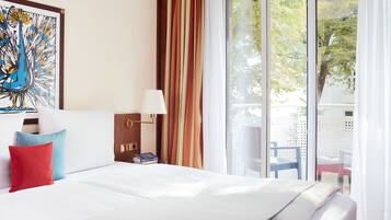 Ein Hotelzimmer mit Bett, Kissen, einer Lampe, einem Gemälde und Blick auf Bäume durch das Fenster.