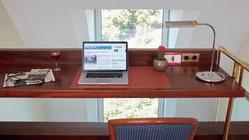 A wooden desk with a laptop, a glass of red wine, a newspaper, a small cactus, and a lamp.