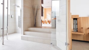 Un baño moderno con cabina de ducha de vidrio, banco de madera y suelo de baldosas.