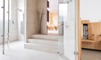 A modern bathroom with a glass shower enclosure, a wooden bench, and a tiled floor.