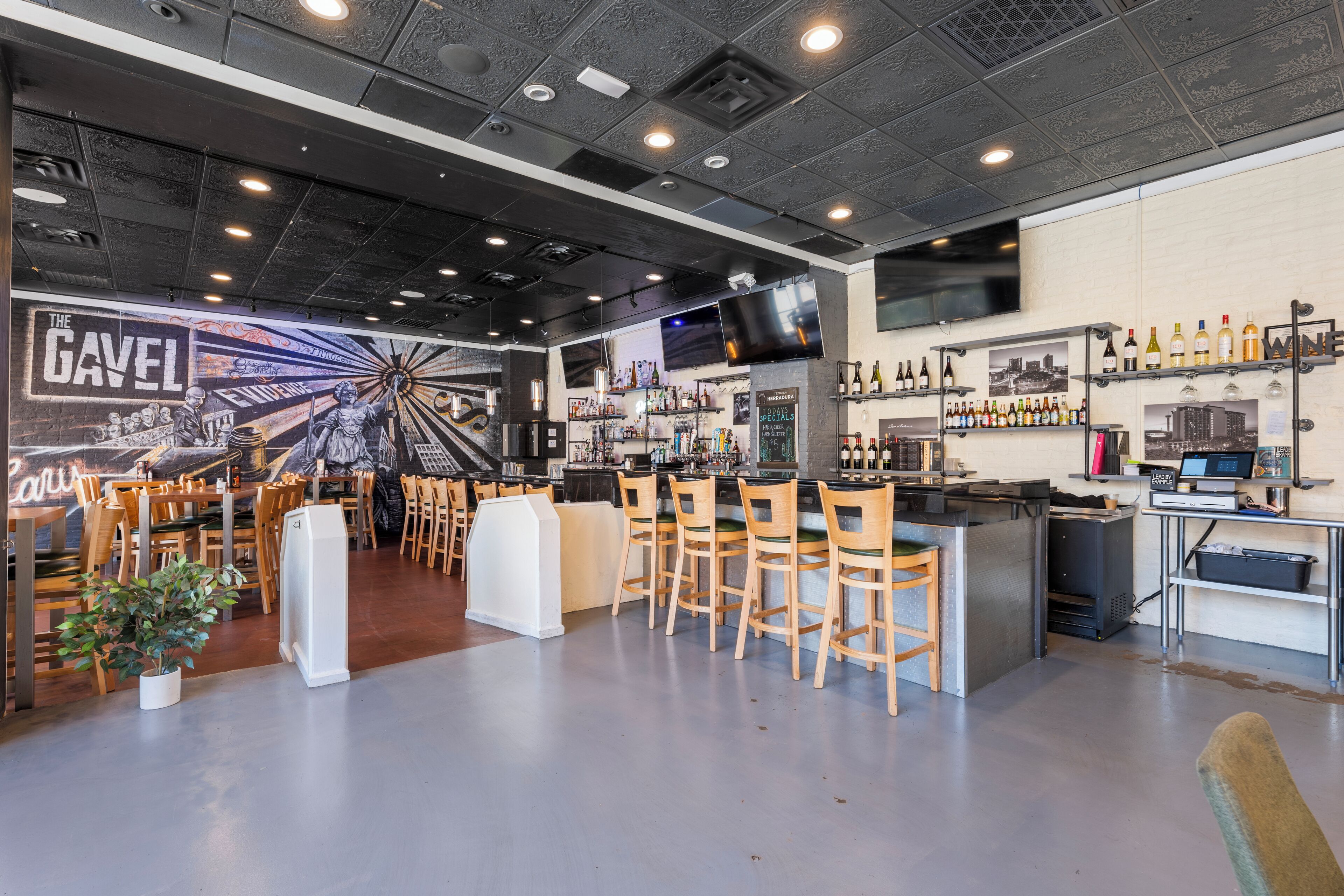 Zona de bar con sillas de madera, una barra y estanterías con botellas.