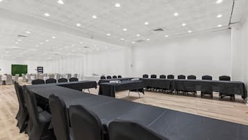 A conference room with long tables, black chairs, white walls, and a wooden floor.