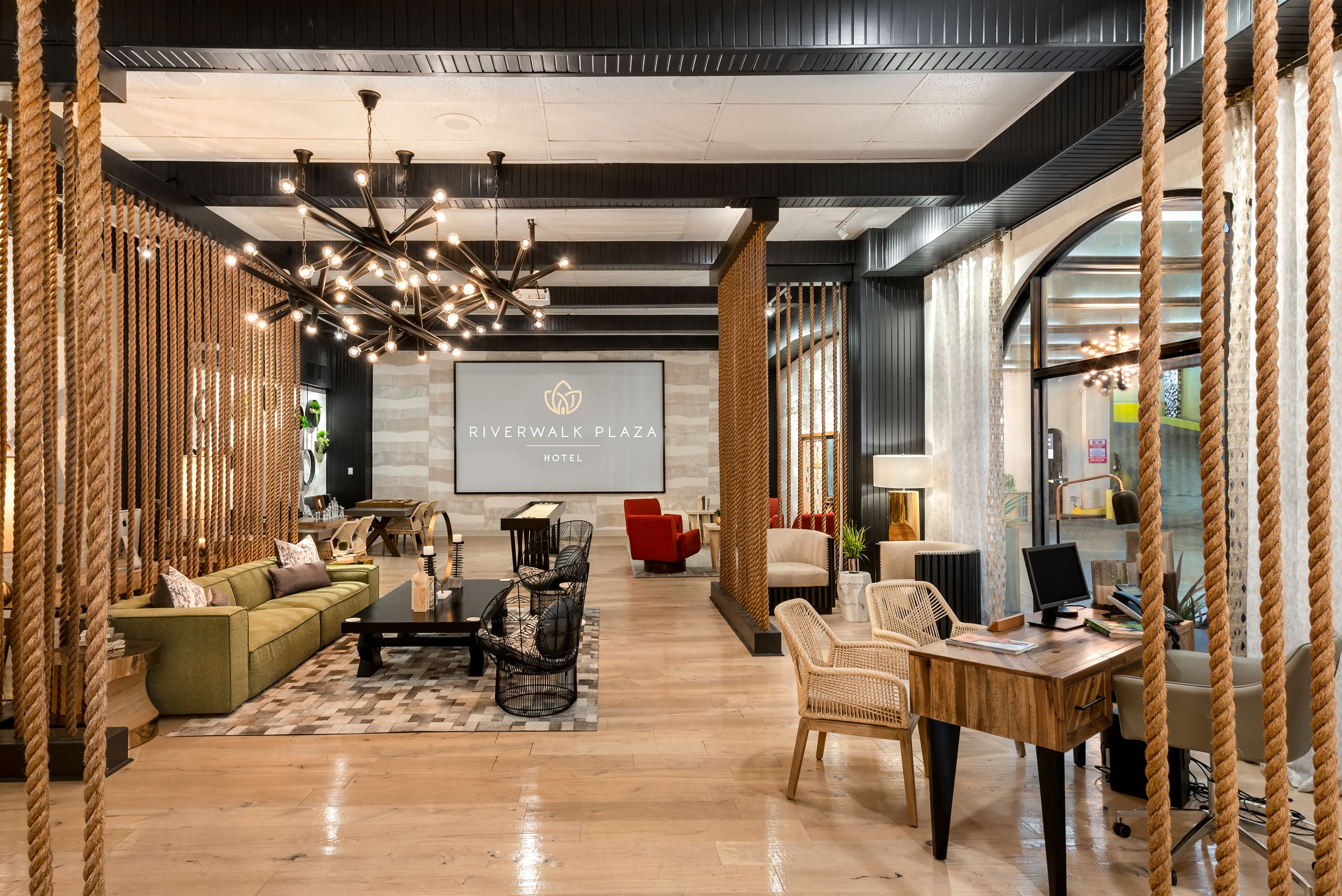 Un moderno vestíbulo de hotel con una pantalla grande que muestra el nombre del hotel, un candelabro y una variedad de zonas de estar, incluyendo sofás y sillones.