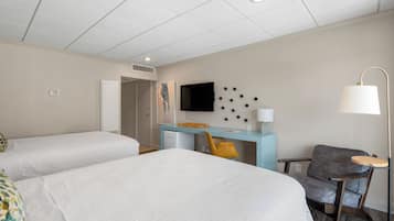 Ett hotellrum med två sängar, ett skrivbord, en stol, en TV och en lampa.