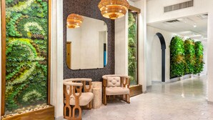 A modern lobby with a large vertical garden, wooden chairs, and a mirror.