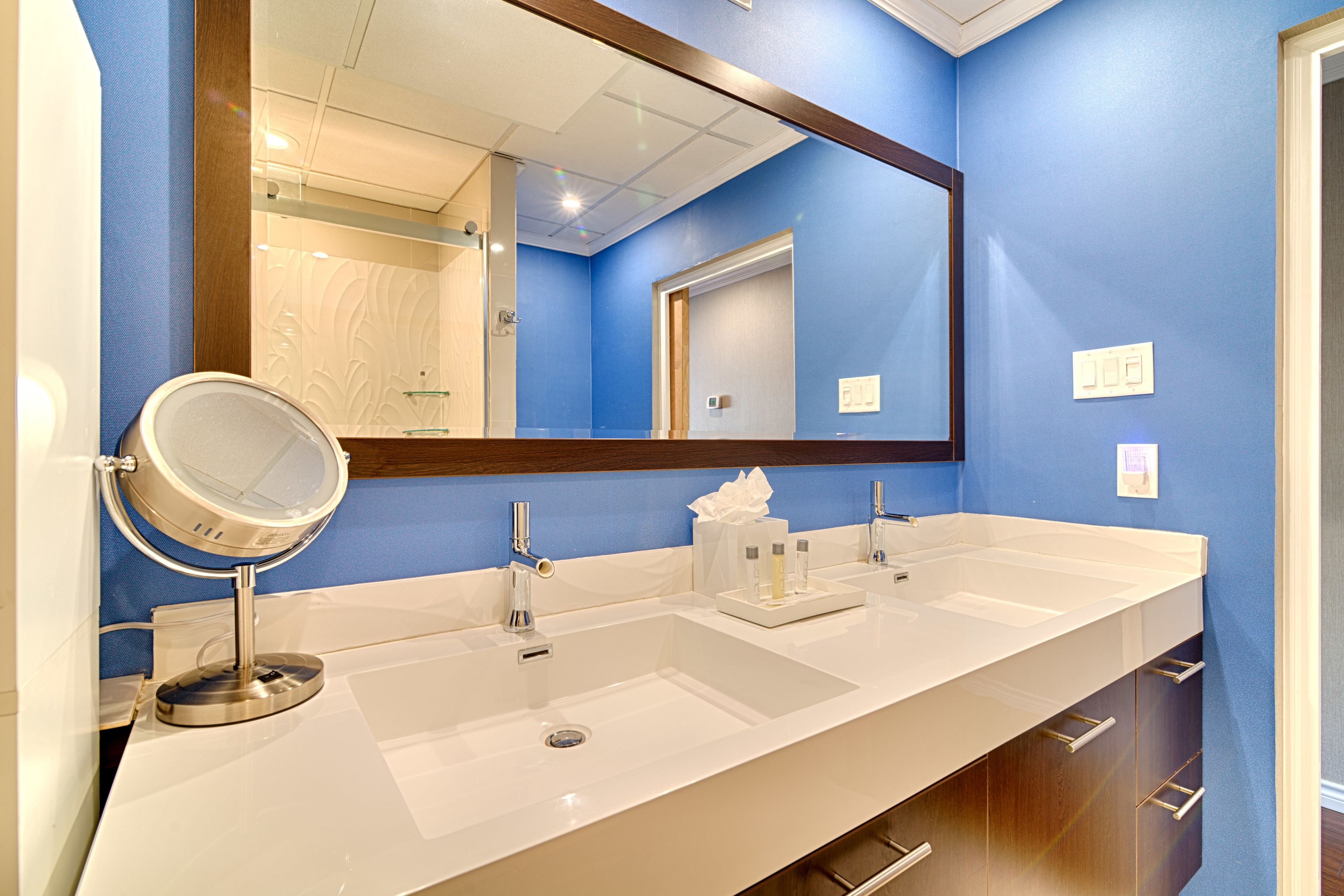 A bathroom with a long white sink, a round mirror, and a large mirror above the sink.